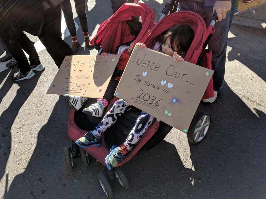 Two siblings hold up signs reading, Watch Out Im Voting in 2036 and Watch Out Im Voting in 2040 at the march in Oakland.