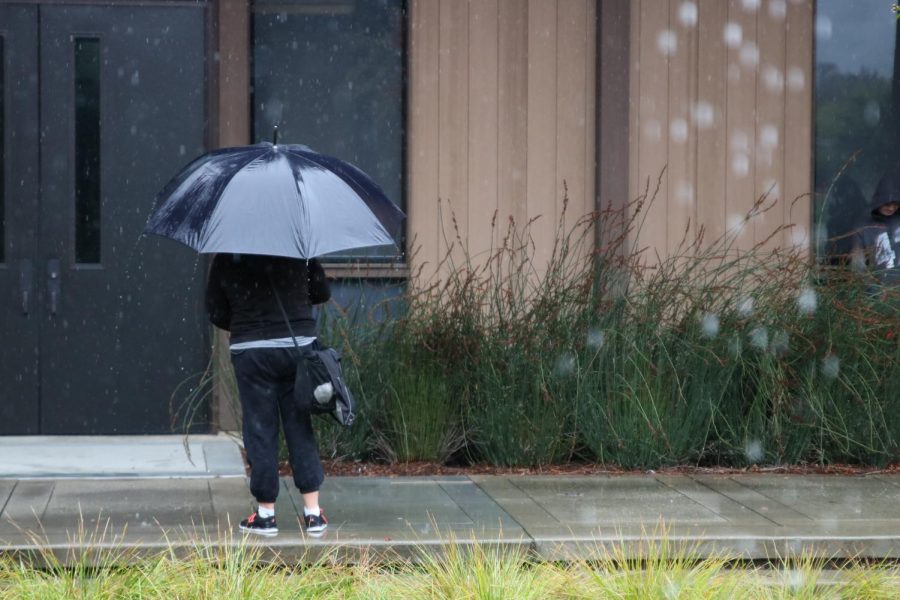 A student stands in the rain in front of a building at Foothill College.