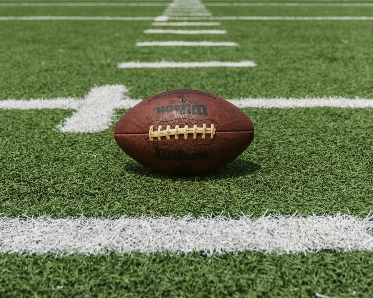 Football positioned on green football field. Photo courtesy of Unsplash.  